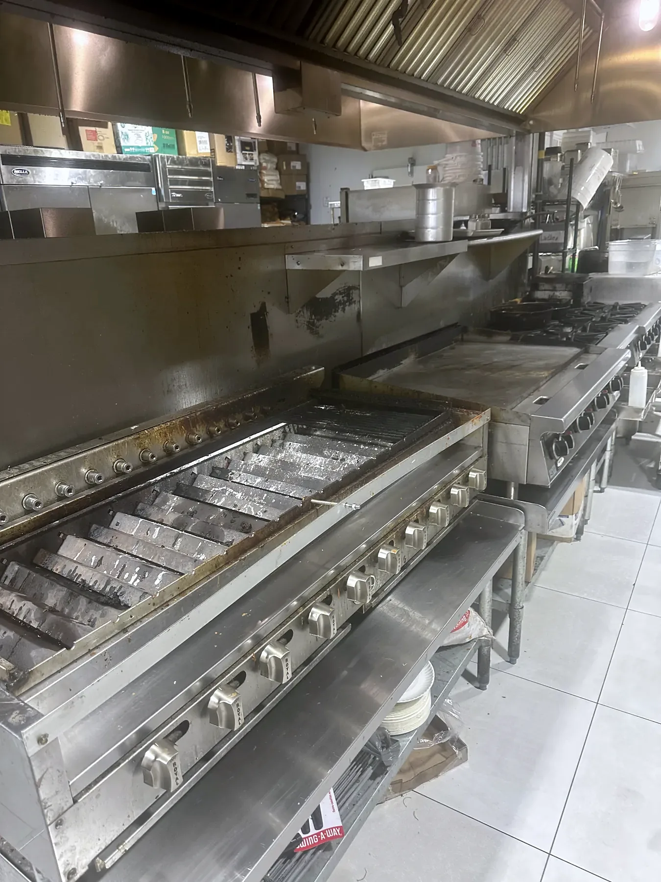 Stainless-steel charbroilers and griddle in a cooking line beneath a commercial exhaust hood