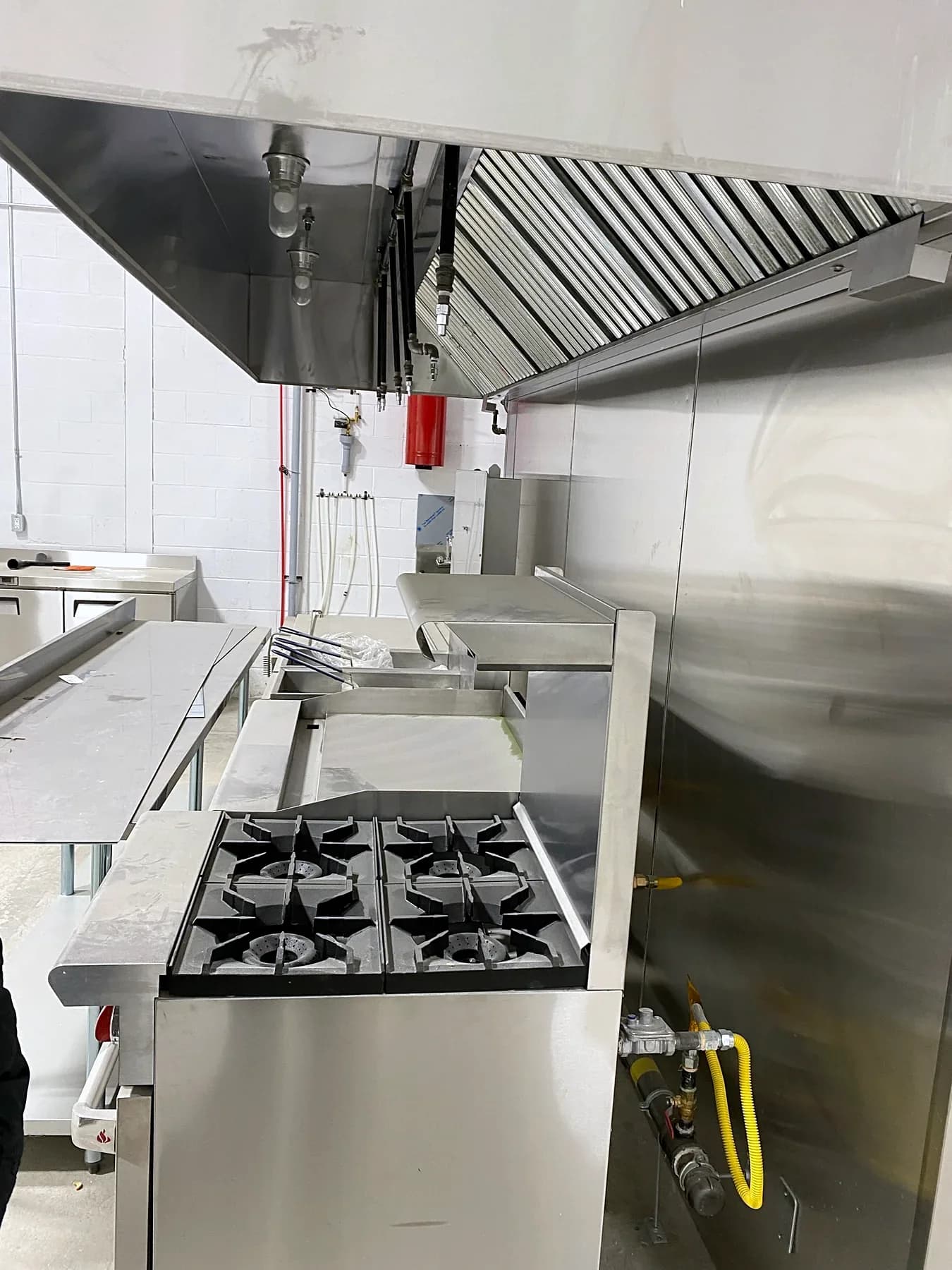 Commercial kitchen cooking line during installation, with a stainless-steel hood, range and visible utility connections