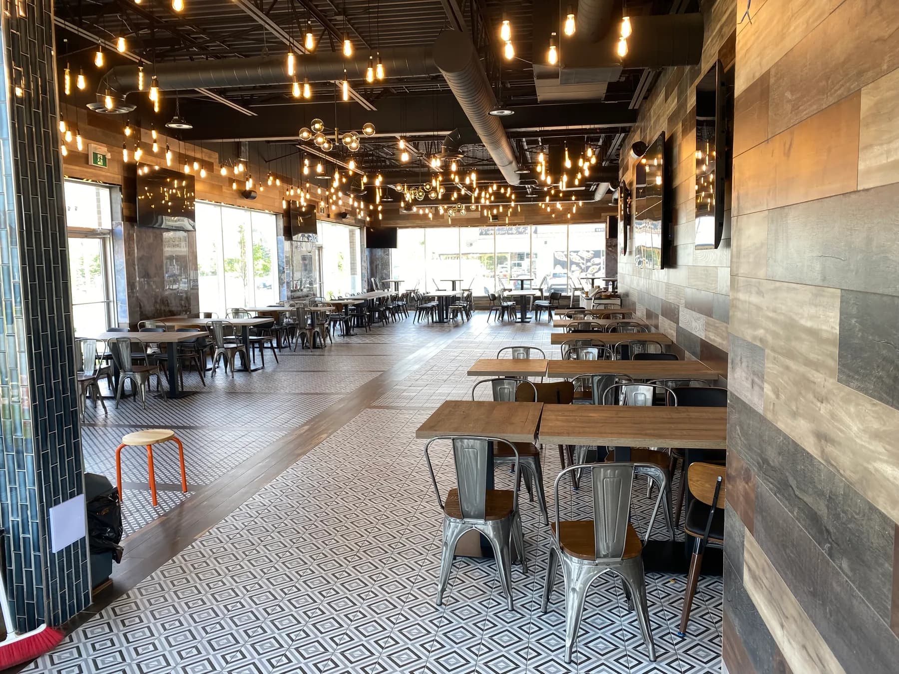 Restaurant dining tables beneath exposed ceiling services and pendant lighting